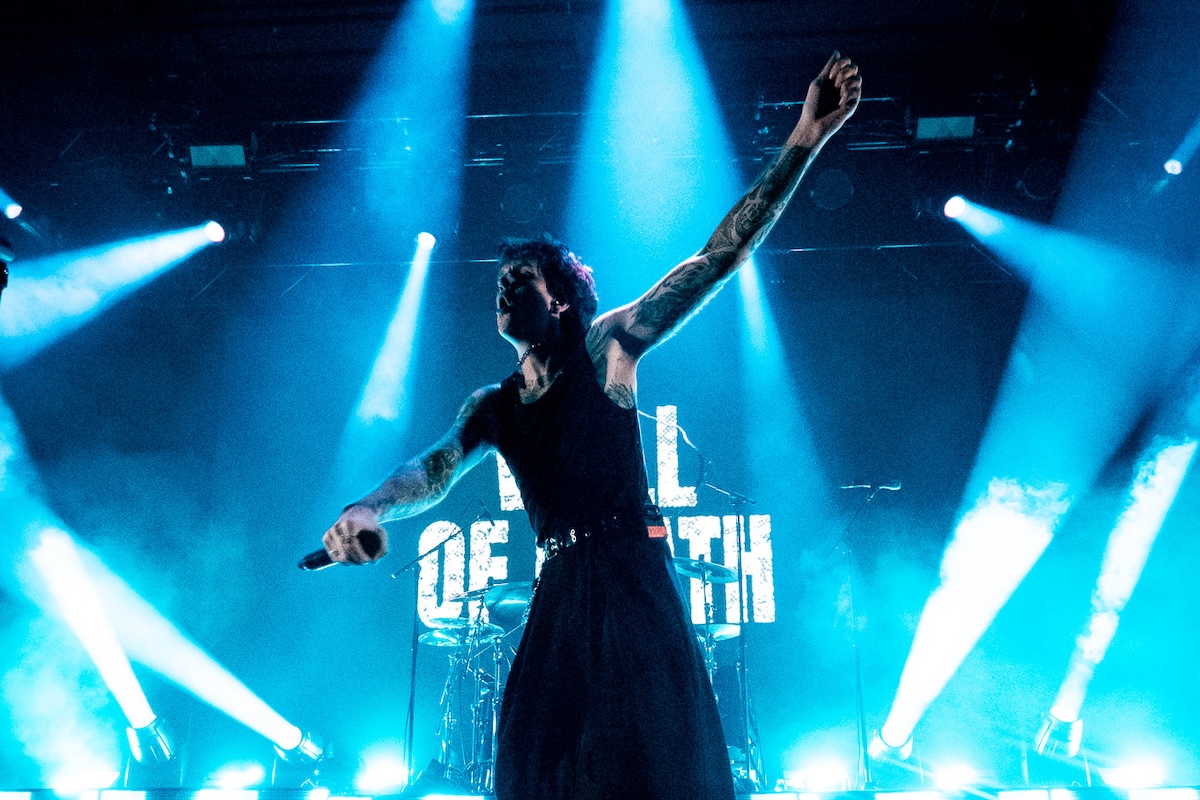 Ocean Sleeper vocalist performing live on stage with arms outstretched under dramatic blue concert lighting and bright stage spotlights.